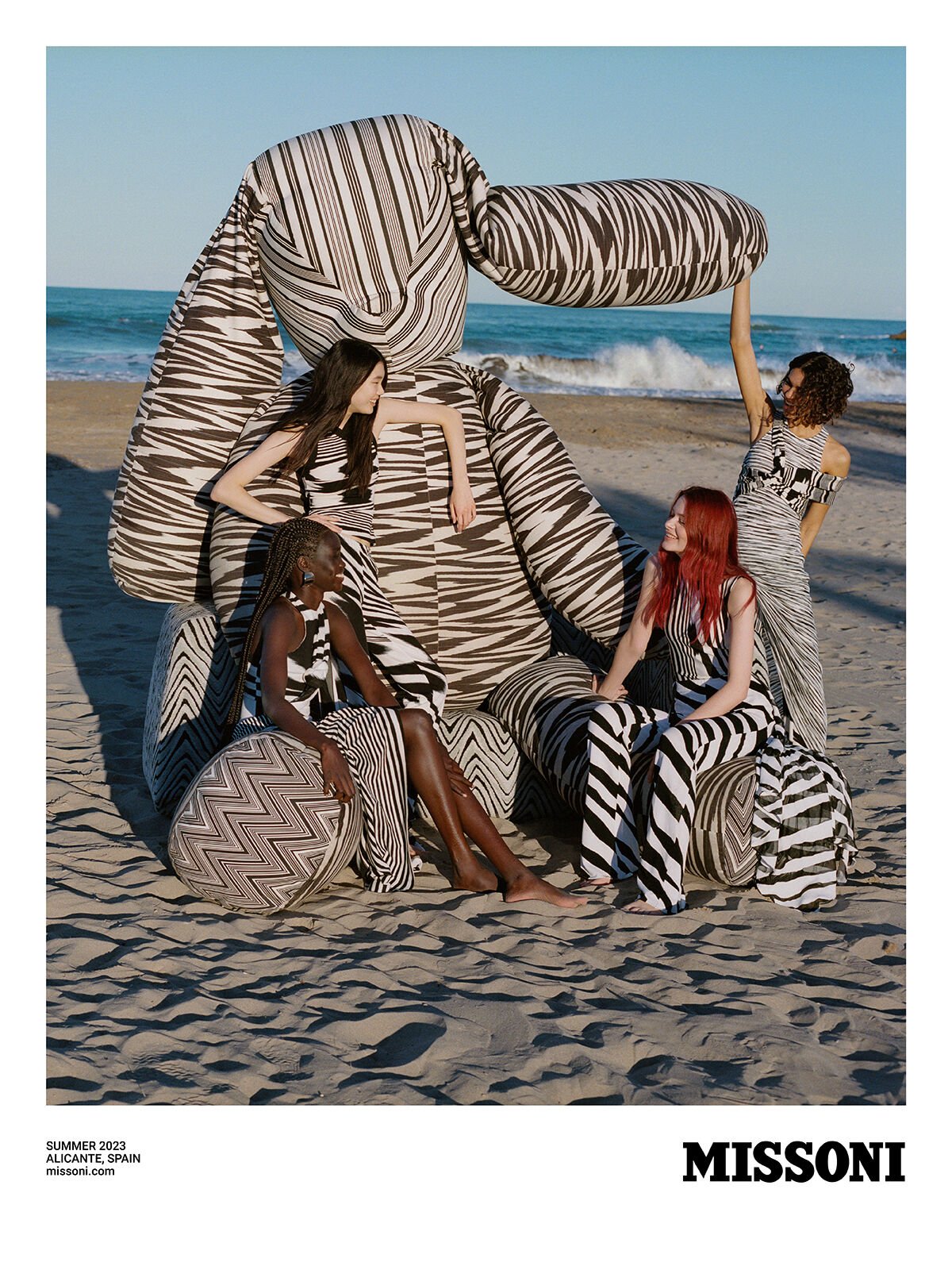 A large knitted rabbit embraces the four models